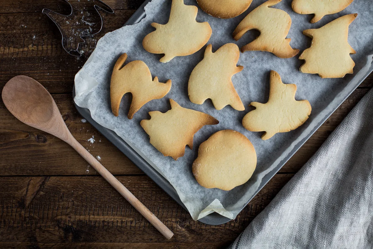 Bandeja de horno con galletas de mantequilla recién hechas en forma de animales, junto a una cuchara de madera