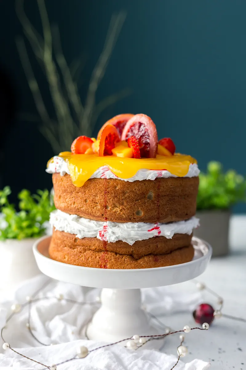 Tarta de dos pisos de bizcocho sin cobertura, con crema y naranja sanguina por encima, sobre un pie blanco