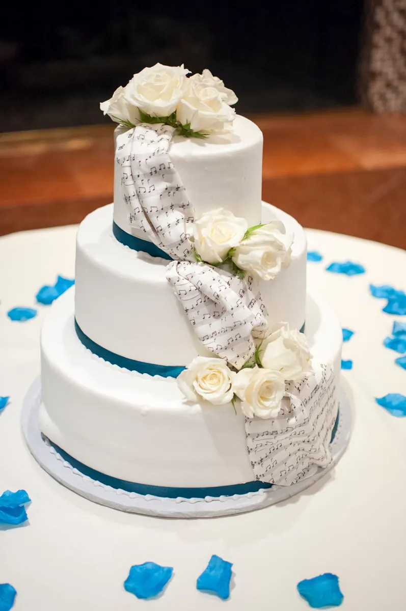 Tarta de boda de tres pisos de fondant blanco con ribete azul y una cascada de rosas blancas